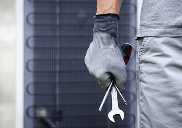 JBL Mechanical technician holding wrenches beside a heat pump coil