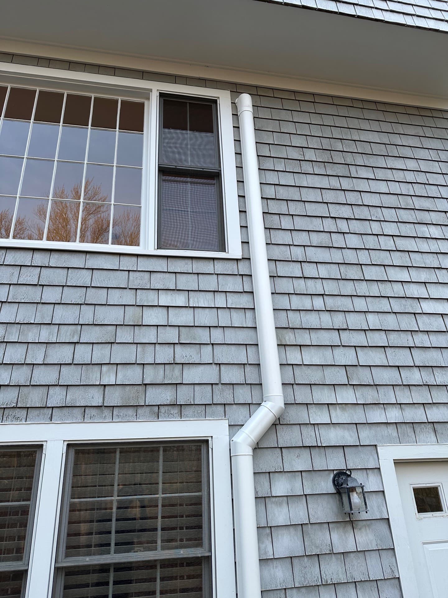Refrigerant line-set cover routed down a shingled wall between two windows