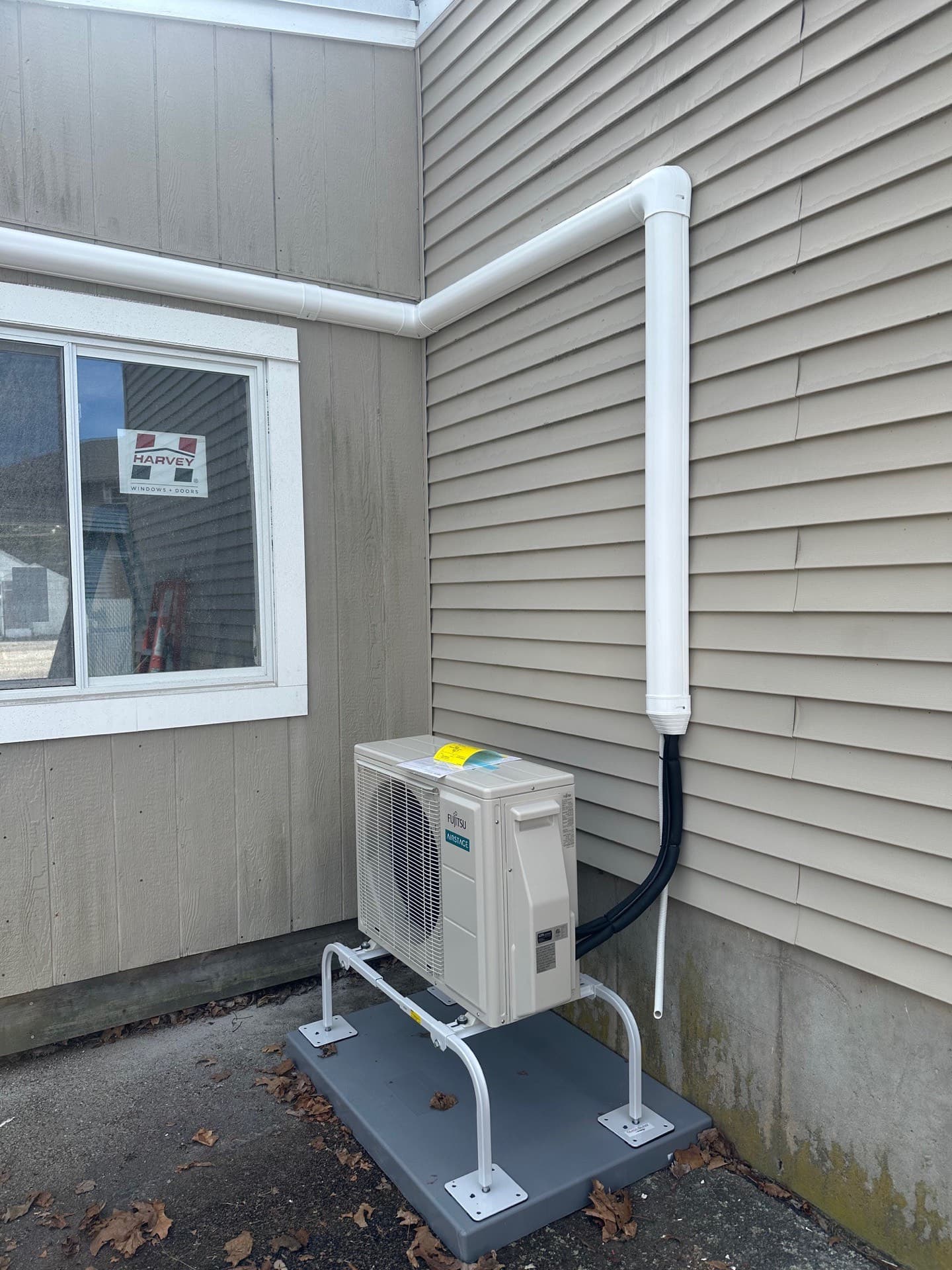 Ductless mini-split outdoor unit on a ground stand beside a vinyl-sided home