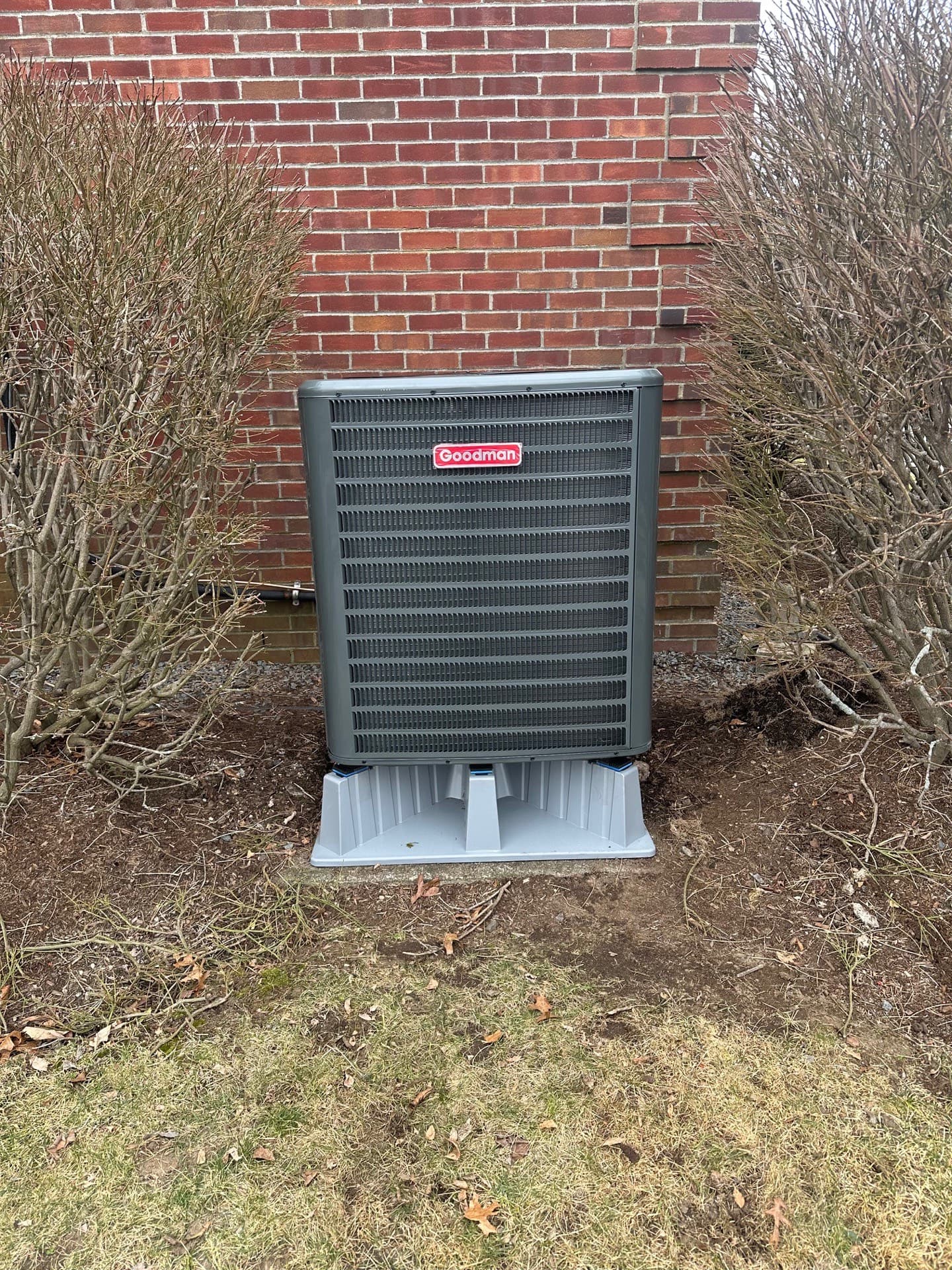 Goodman condenser set on a composite pad against a brick exterior wall