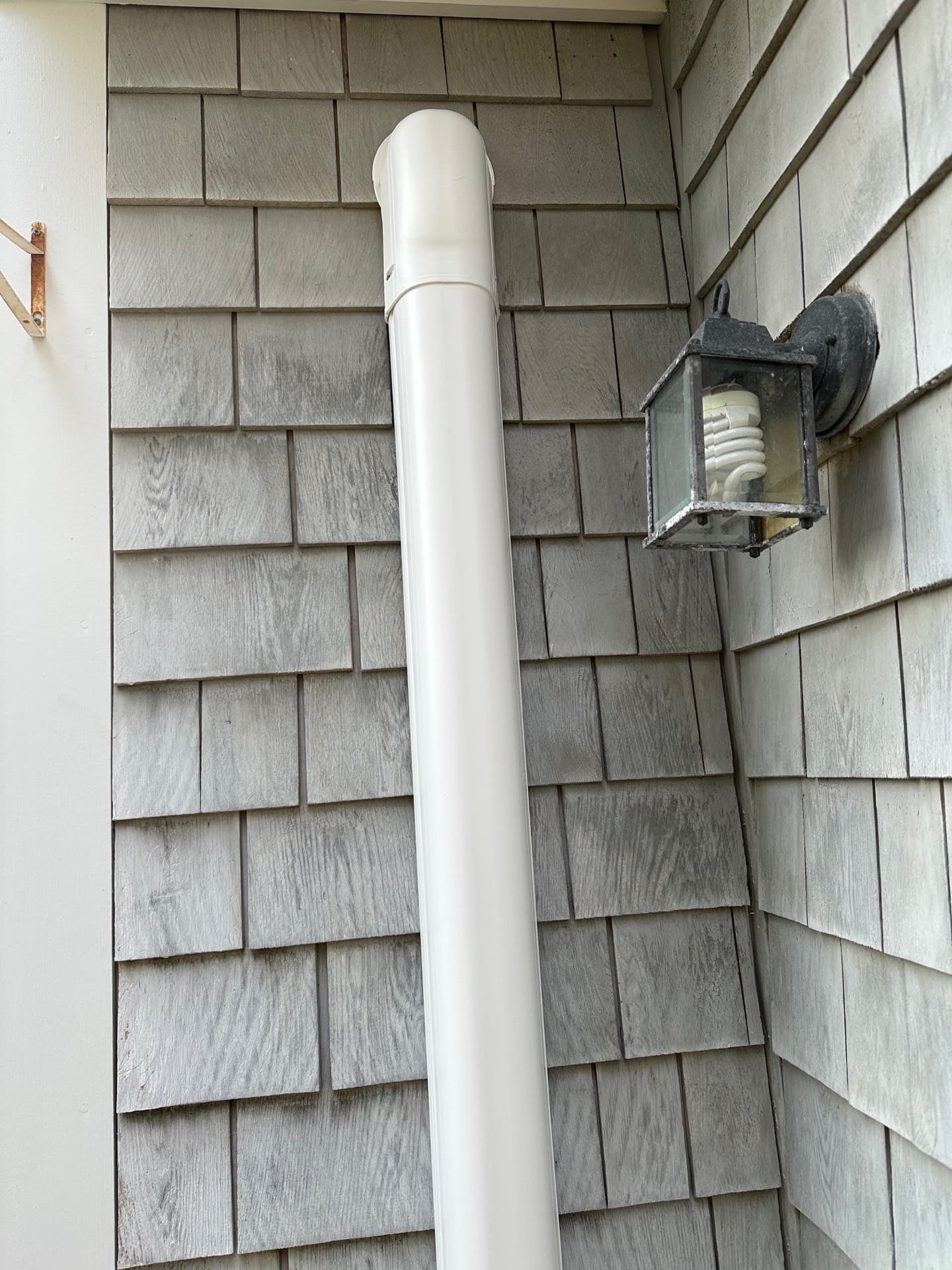 Line-set cover run down a shingled wall past an exterior light fixture