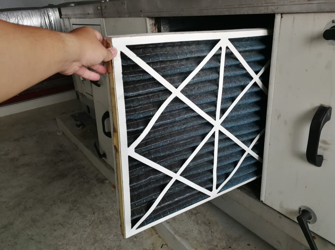 Technician sliding a clean pleated filter into a home air handler