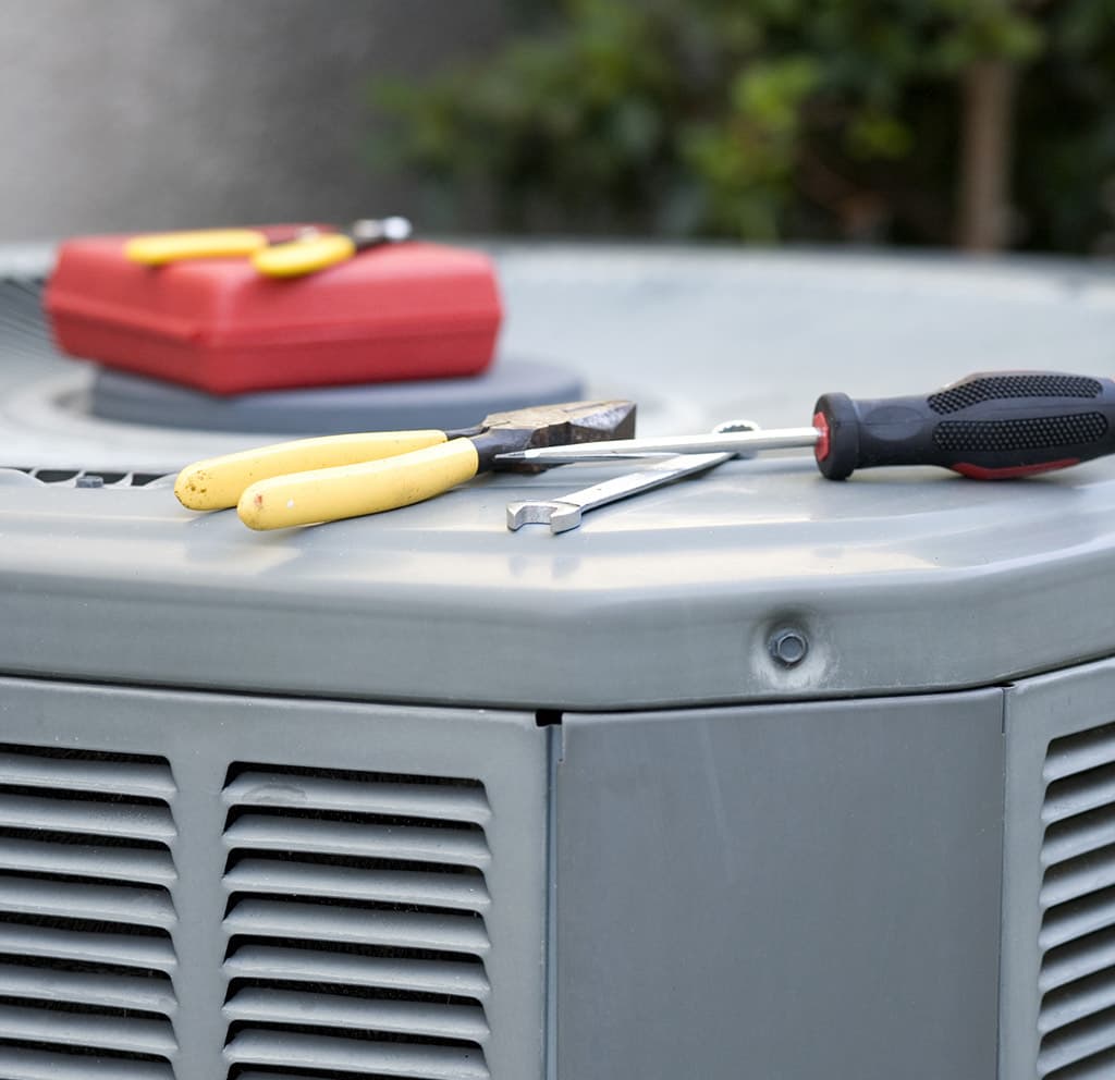 Technician's tools laid out on an outdoor AC condenser during maintenance